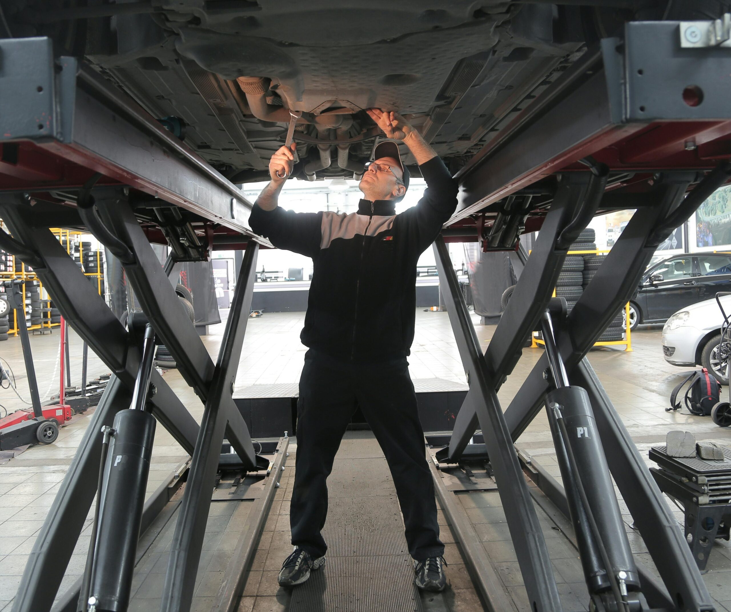 Een monteur voert reparaties uit aan een auto die op een hefbrug staat.